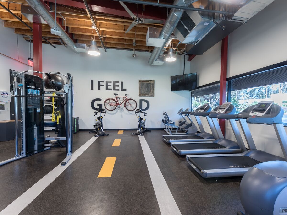 academia moderna com esteiras, bicicletas de spinning, equipamento de musculação e decoração criativa com bicicleta na parede e frase 'i feel good